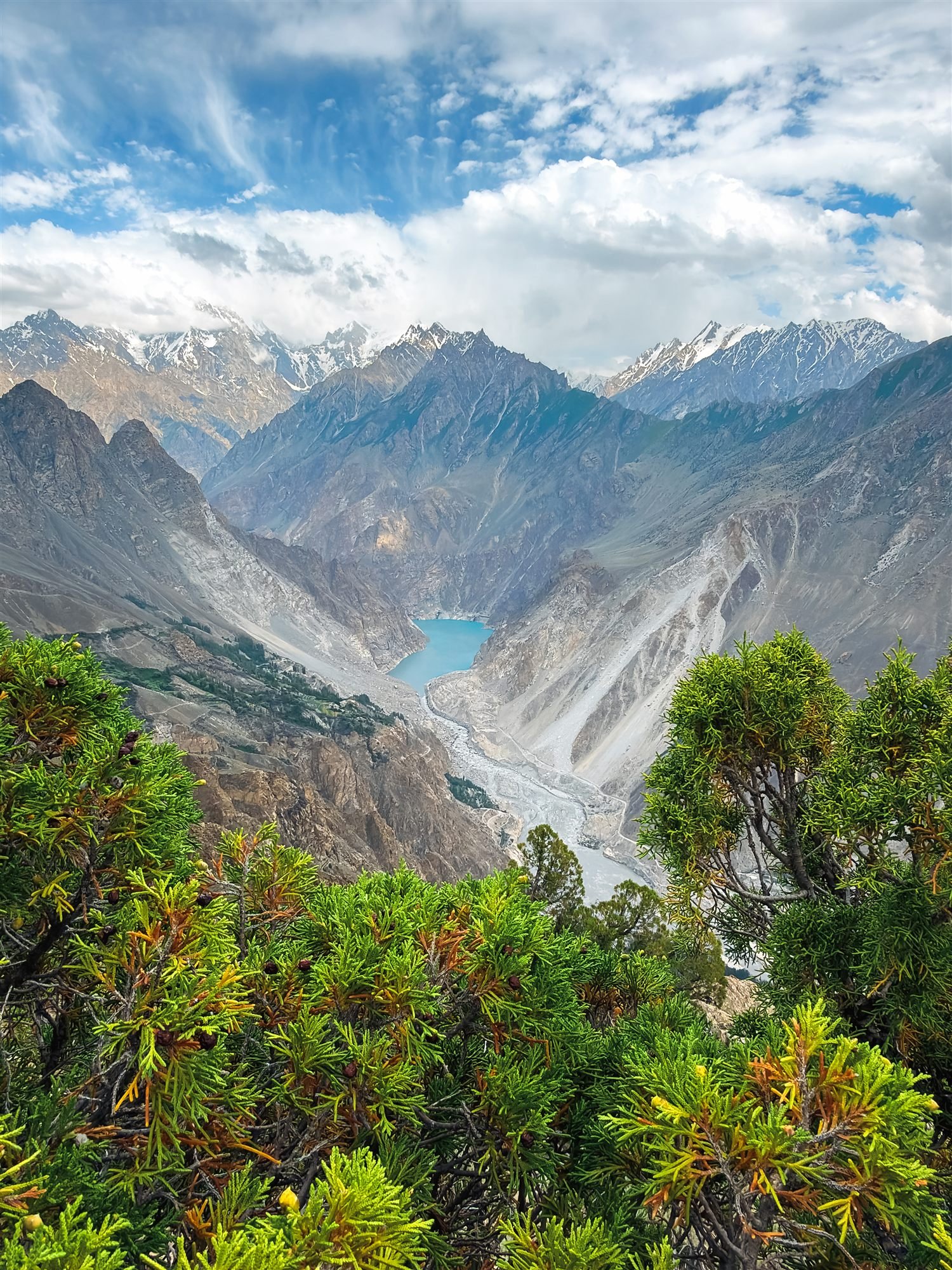 The turquoise water of Attabad Lake seen from above through juniper branches