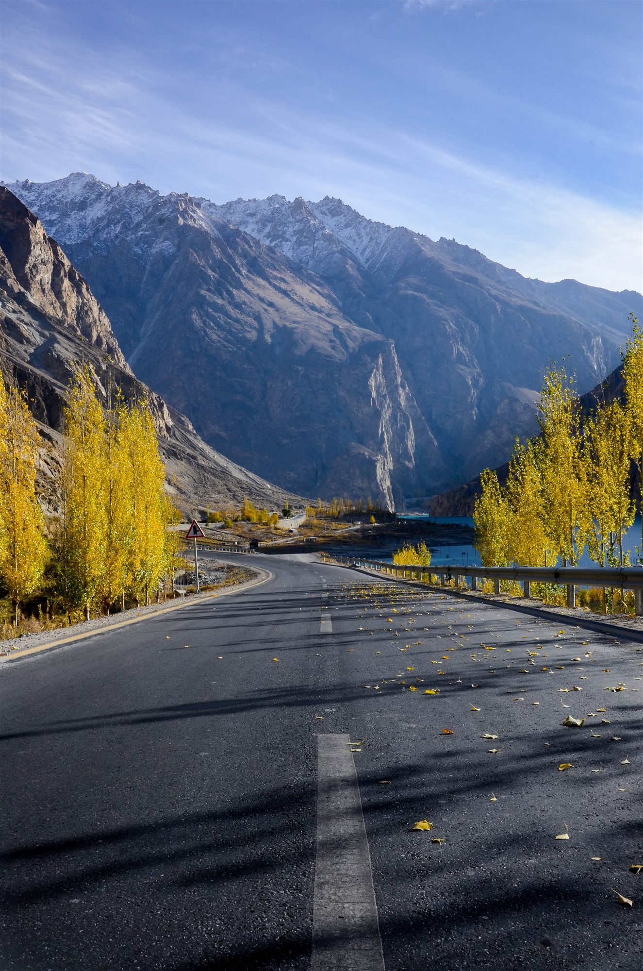 The Karakoram Highway lined with golden poplars in autumn beside a turquoise lake