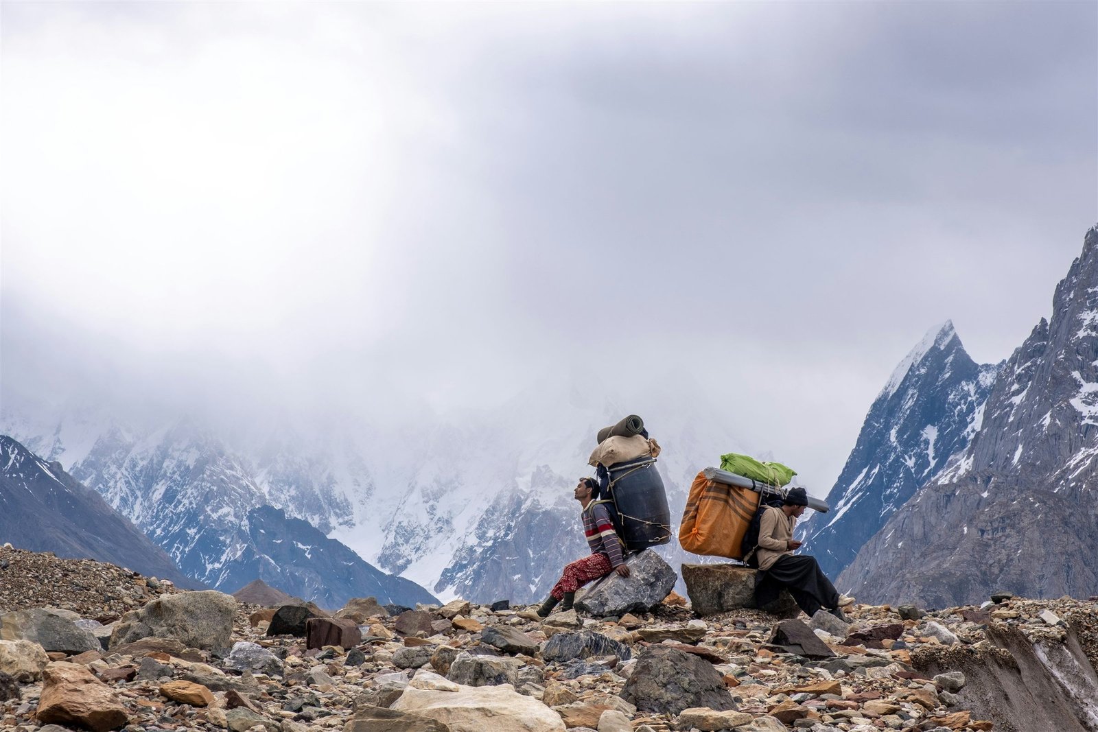 A porter with a load on the Baltoro glacier, peaks rising through cloud beyond