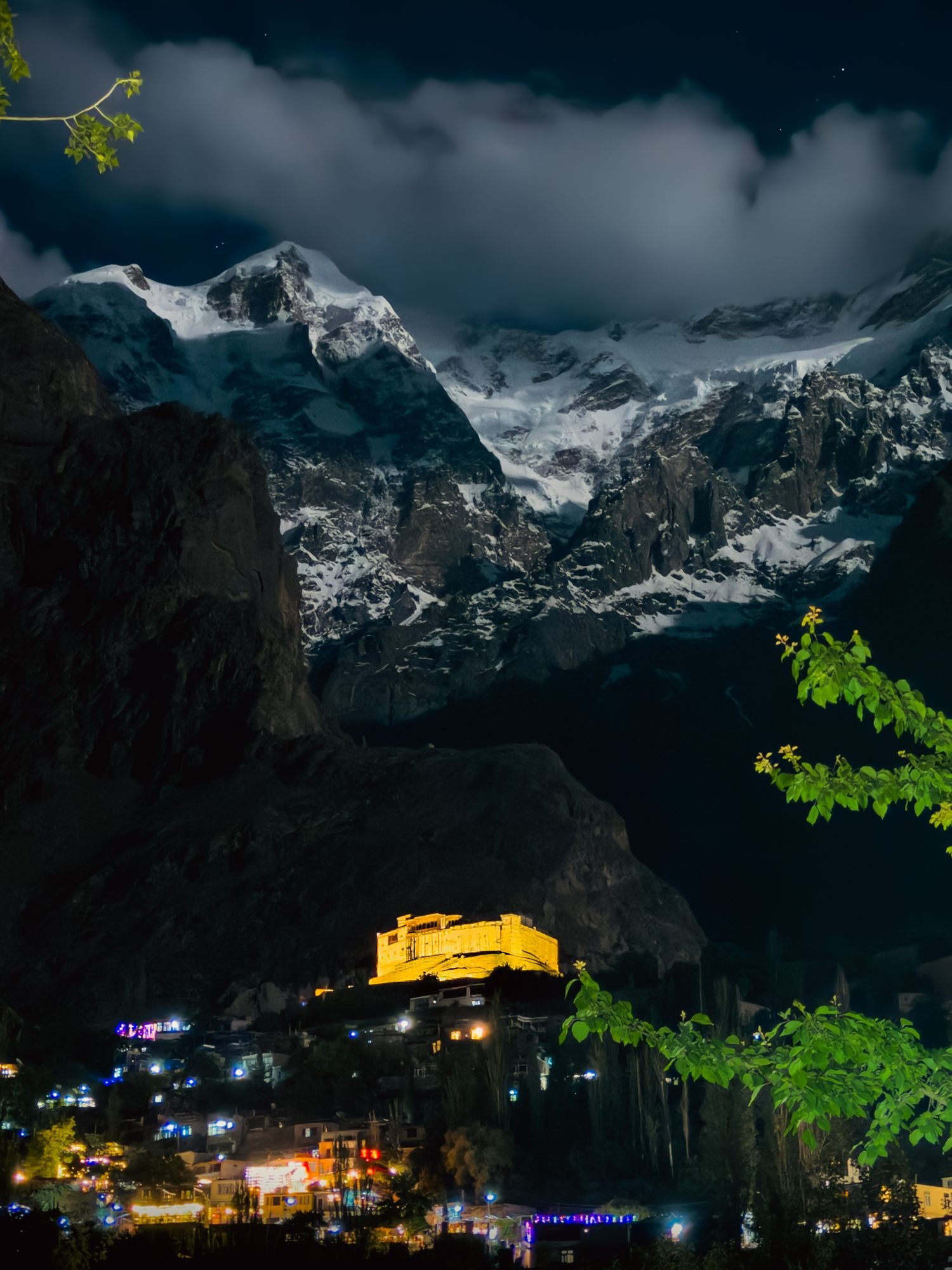 Baltit Fort lit gold at night beneath a snow peak above Karimabad