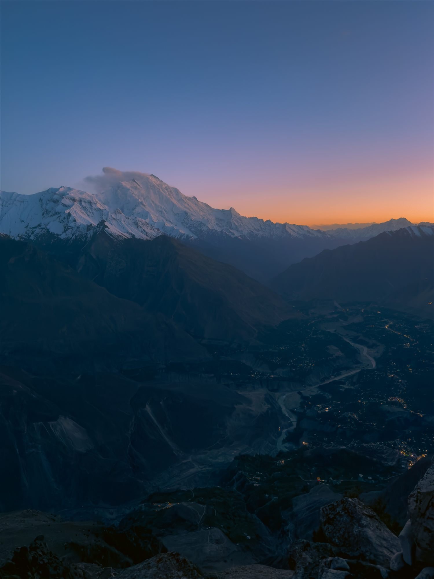 Karimabad at dusk, lights coming on in the valley beneath a snow peak