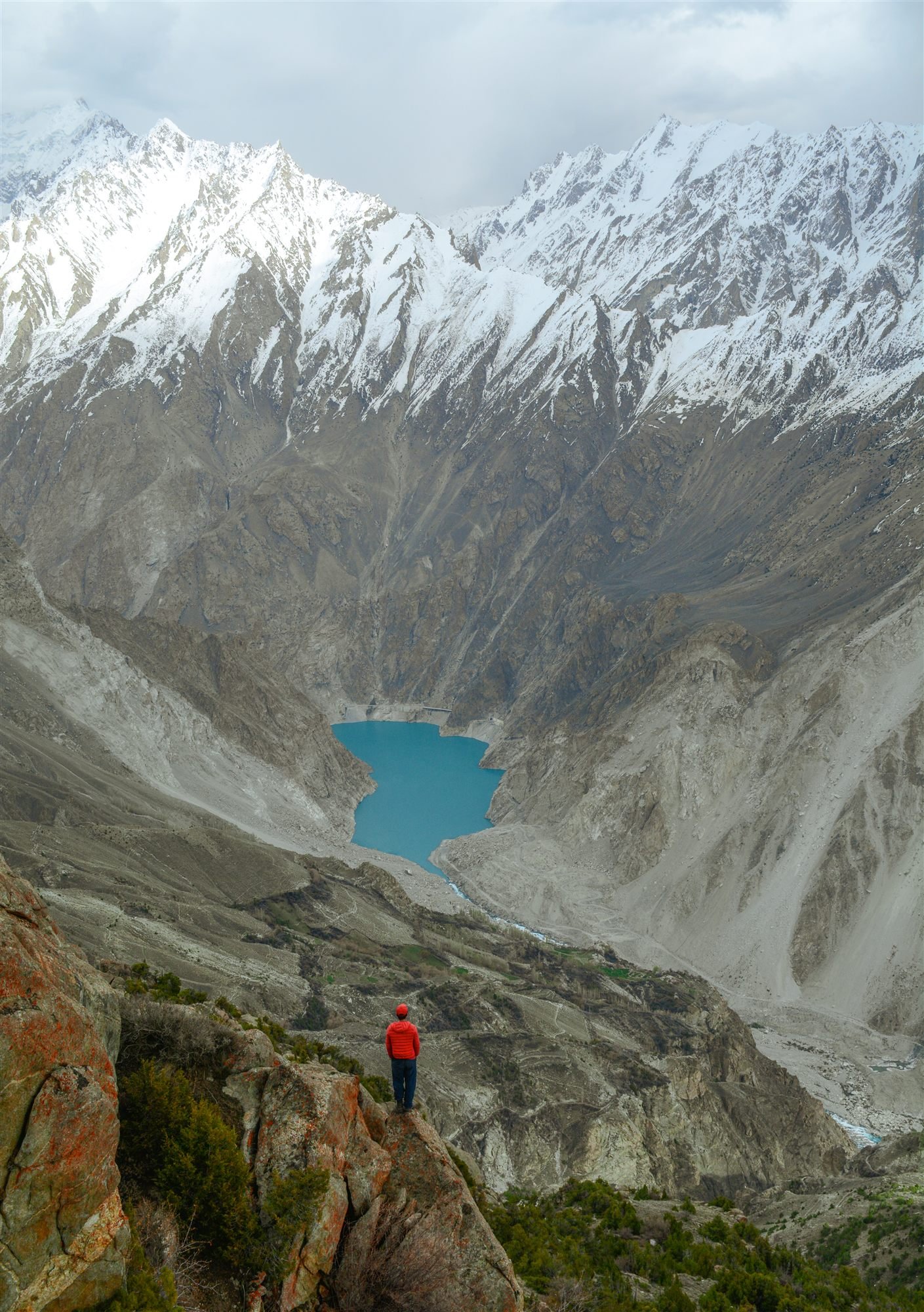 A traveller looking down at Attabad Lake from a rocky viewpoint above the valley